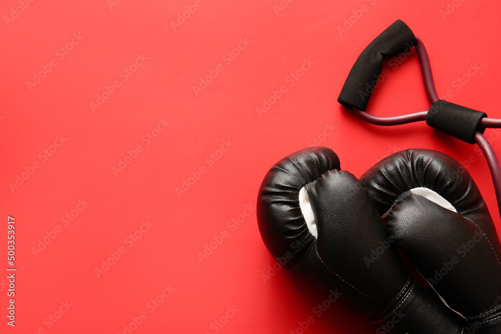 Fitness expander and boxing gloves on red background