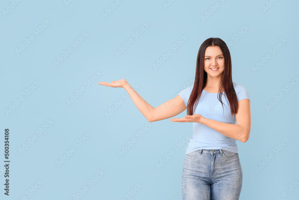 Young woman in t-shirt showing something on blue background Young woman in t-shirt showing something on blue background