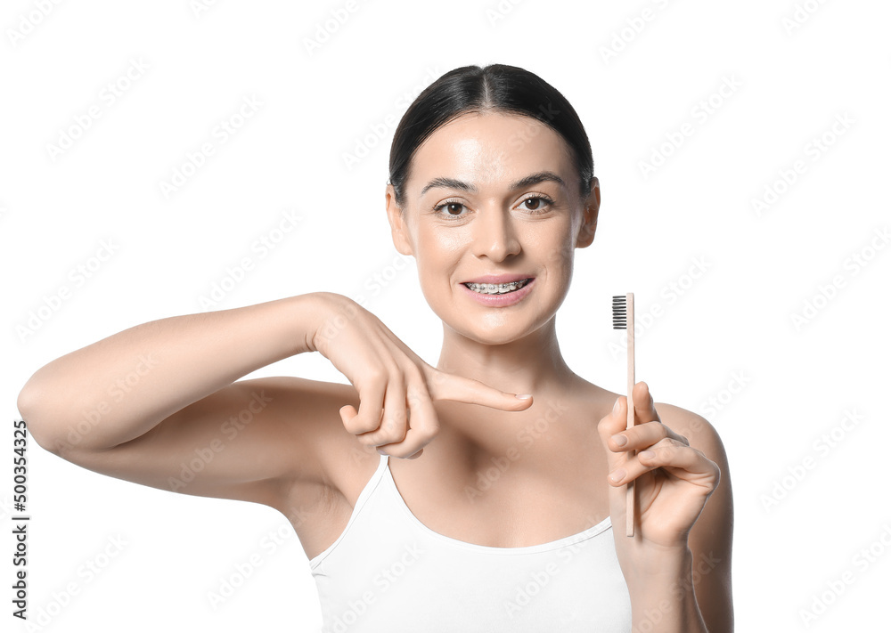Beautiful woman with dental braces pointing at toothbrush on white background Beautiful woman with dental braces pointing at toothbrush on white background