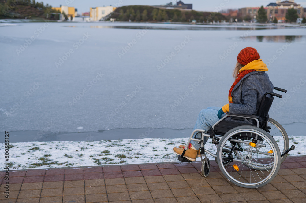 Caucasian woman in a wheelchair walks by the lake in winter.