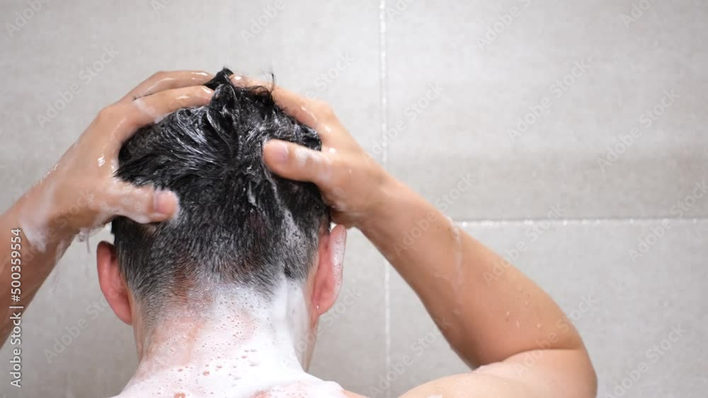 Male hand washes his head with shampoo and foam on gray background close-up, back view. Male hand washes his head with shampoo and foam on gray background close-up, back view.