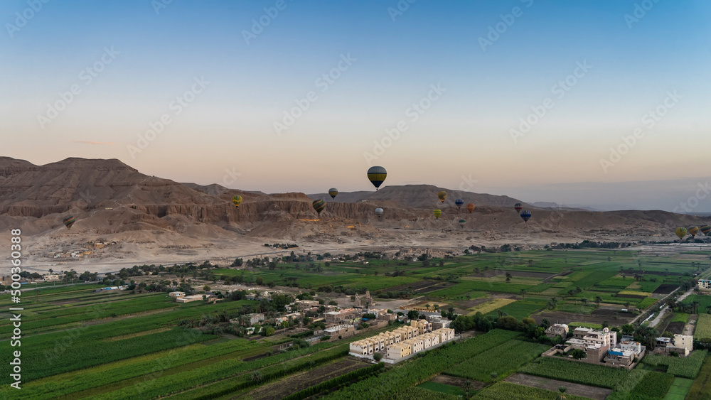 Balloons are flying over the Nile Valley. Below you can see green plantations, village houses. A mountain range against the background of the morning sky. Egypt. Luxor