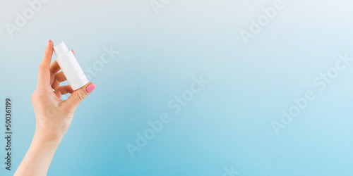 Banner a woman's hand holds a white tube with a cosmetic product on a blue background. Beauty product concept. Sample.