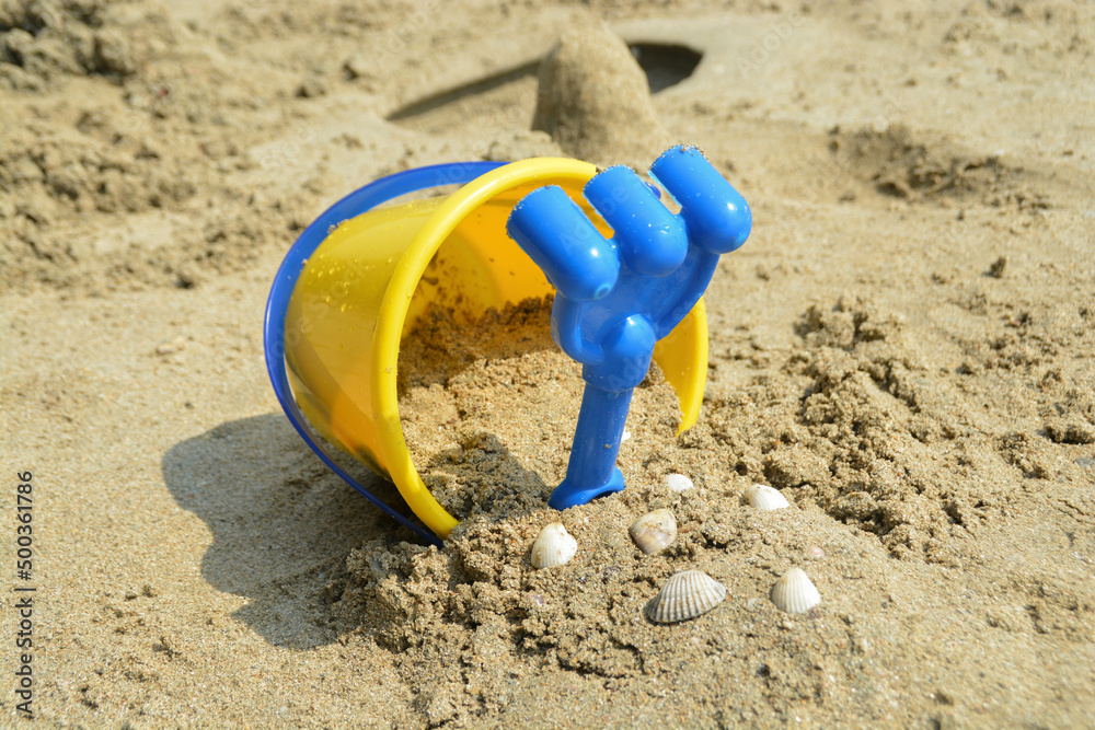 Yellow bucket kids toy and blue rake. And sand in the bucket with some shell. Yellow bucket kids toy and blue rake. And sand in the bucket with some shell.