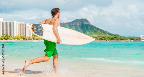 Hawaii surfing lifestyle young man sufer going to surf in blue ocean water in Honolulu, with Diamond Head in background. Oahu island travel vacation