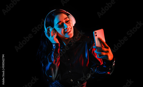 latin young woman with headphones listening to music over color neon and black background in Mexico Latin America	