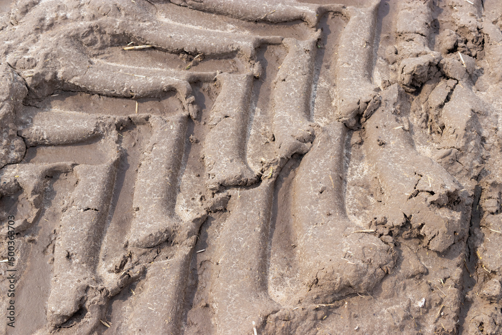 Footprint of wheel tread on the ground road. The trail from the tread of trucks wheels. Car tire tread imprint on sand, background, texture. Footprints rubber tyres from automobile. Close-up. Footprint of wheel tread on the ground road. The trail from the tread of trucks wheels. Car tire tread imprint on sand, background, texture. Footprints rubber tyres from automobile. Close-up.