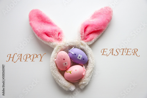 Decorative Easter eggs in a tray on a white background with fluffy rabbit ears, with the text HAPPY EASTER. Holiday concept