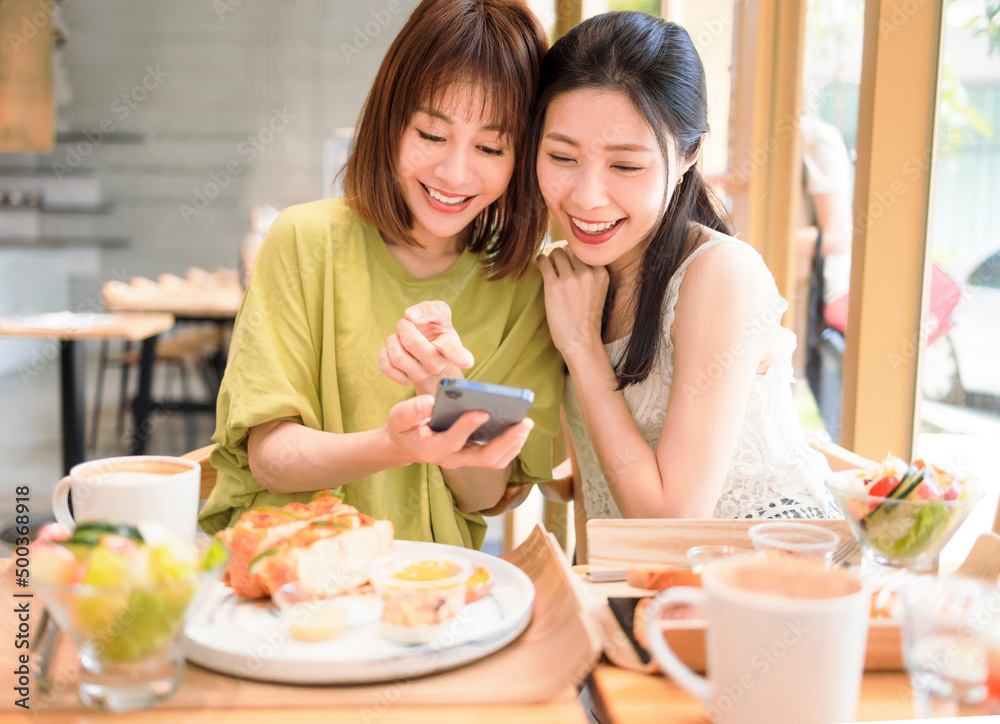 Young women sitting in restaurant looking at mobile phone and smiling Young women sitting in restaurant looking at mobile phone and smiling