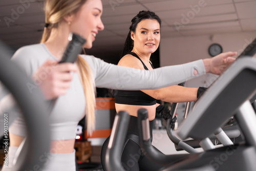 two attractive athletic young women are training together in the gym. Perform exercise on cardio machine.