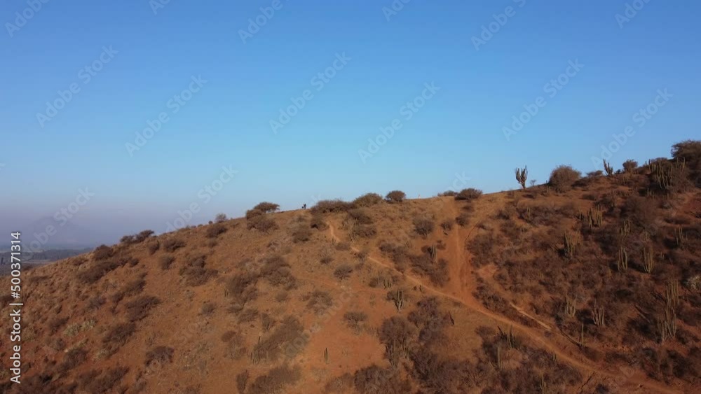 Dry hills with cacti show the lack of rain. Town and locality located in valley. Families climbing to the top of the hill. 4k