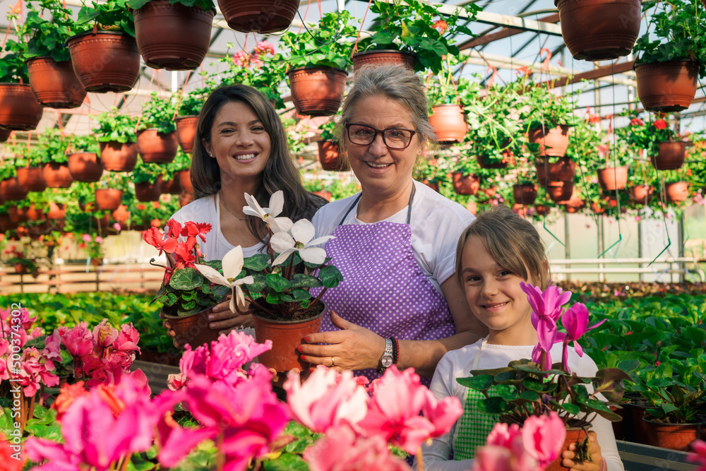 Grandmother, mother and daughter posing for photo while holding flowers in greenhouse.