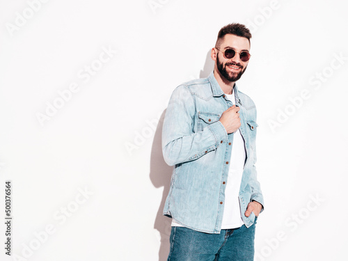 Portrait of handsome confident stylish hipster lambersexual model.Man dressed in jacket and jeans. Fashion male posing near wall in studio in sunglasses. Isolated © halayalex