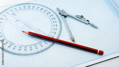 On blue graph paper are compasses, protractor, ruler, and a pencil