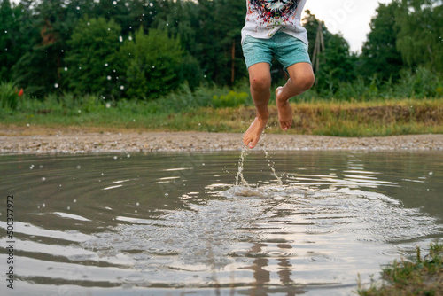 Fototapeta Naklejka Na Ścianę i Meble -  A cheerful child runs through the puddles after the rain on a warm day