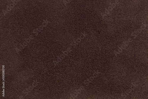 Background of dark brown suede matte fabric. Velvet matt texture of umber nubuck textile. Velveteen pattern.