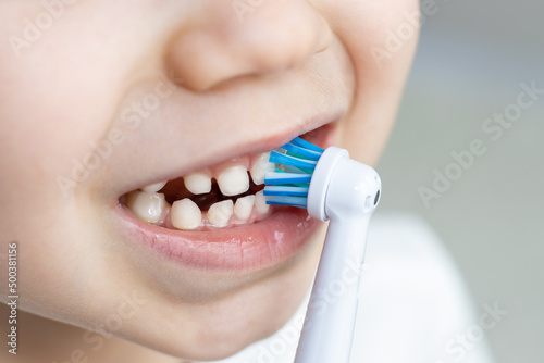 cute kid is brushing his teeth with an electric brush teeth. close up of child's mouth, rare teeth with multiple diastema. excited happy boy and daily routine, dental hygiene concept. 