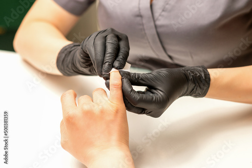 The manicurist finishes the procedure for red nail polishing and cleaning with a cotton napkin  pad  swab in a beauty salon  close up