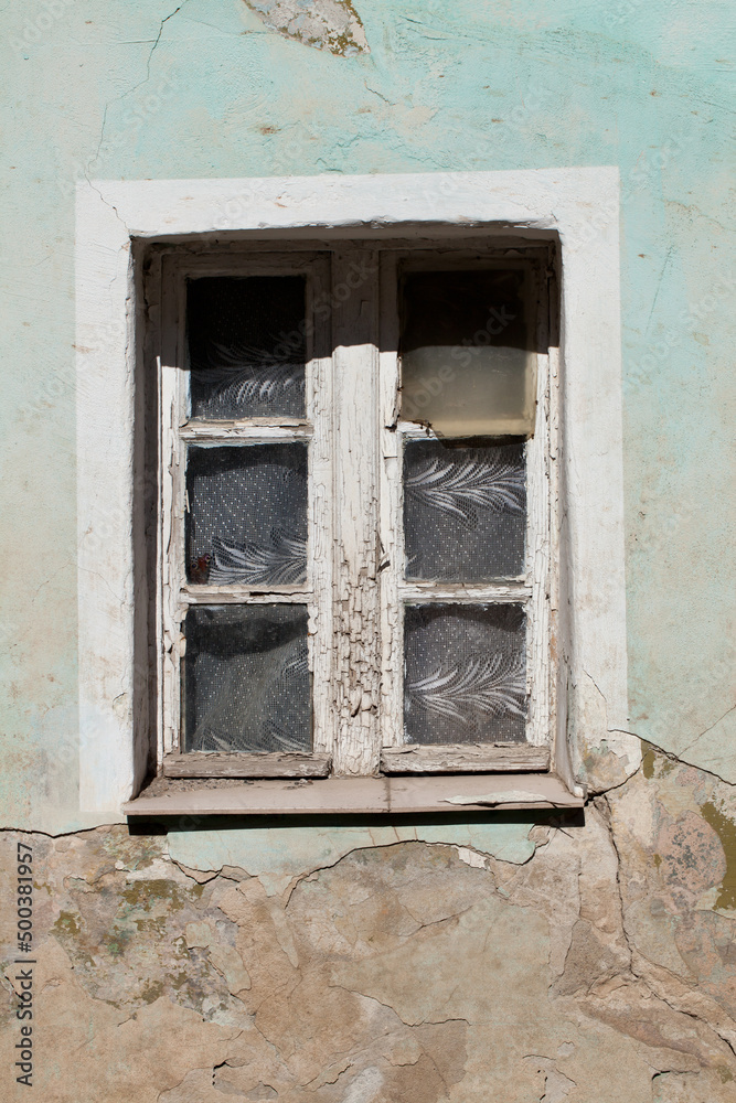 An old wooden window and a dilapidated and cracked wall of a rural building.