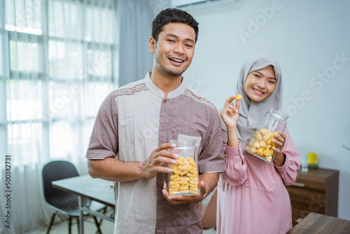 muslim couple holding idul fitri snack in the jar at home kitchen photo