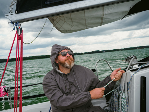 sailing on a yacht in rainy weather. adult man using a winch to pull a rope on a sailboat or sailing yacht to control a yacht sail, the yacht sails in a thunderstorm on a rainy autumn day