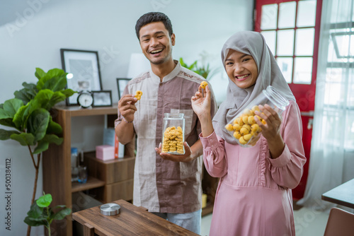 muslim couple holding idul fitri snack in the jar at home kitchen