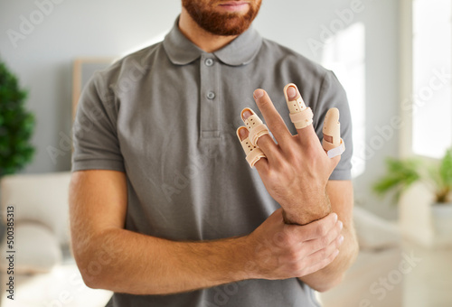 Man wearing adjustable finger splint braces. Cropped close up shot of a young guy showing his hand with beige support braces on his injured fingers and thumb. Concept of injury treatment photo