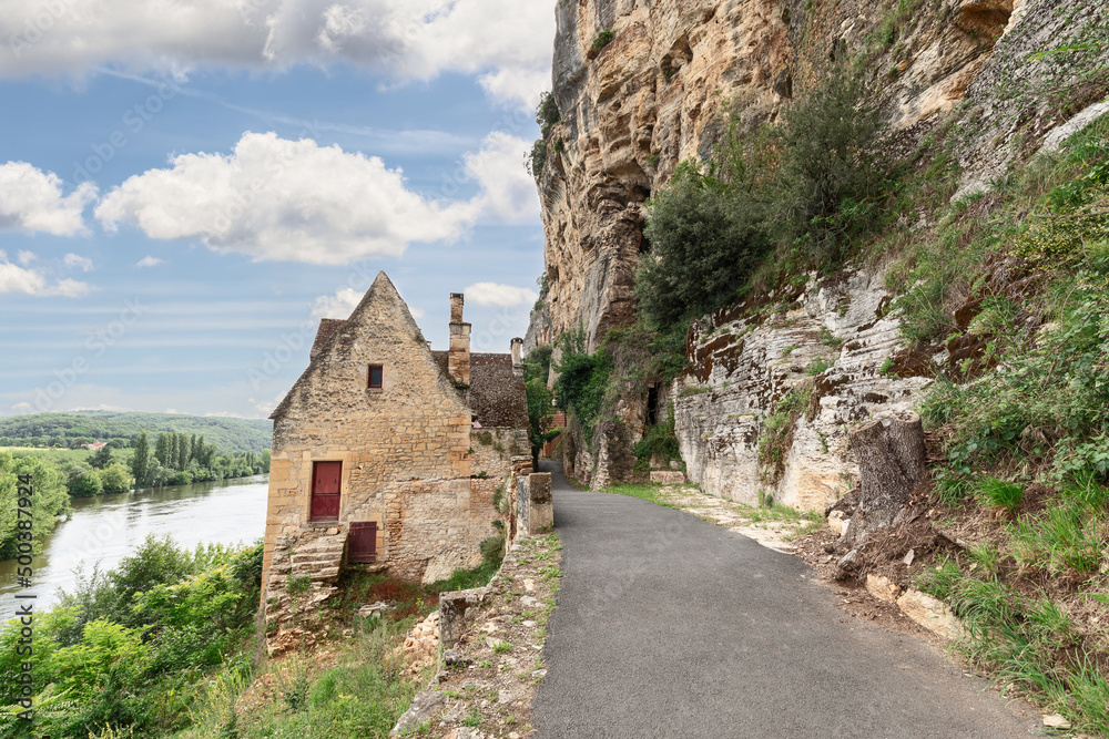 Secluded stone house on road along steep cliff on one side and full-flowing bed of Dordogne river. Dordogne department, New Aquitaine region, France