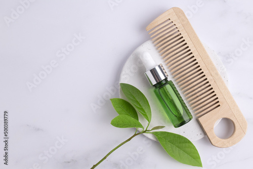 Cosmetic glass bottle with dropper  wooden hair comb and green leaves on podium. The concept of a beauty salon and natural cosmetics.