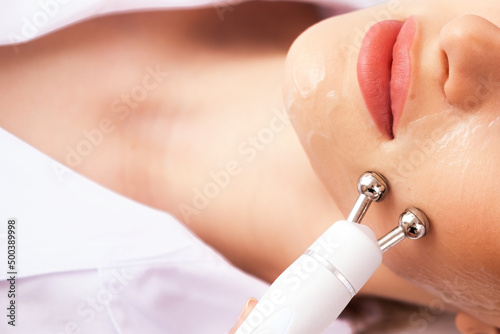 Close-up portrait of a beautiful woman with closed eyes and apparatus for skin rejuvenation. Beauty salon procedures. RF lifting. Microcurrents. photo