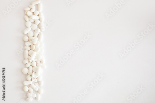 Biała tabletka trzymana w dłoni, białe lekarstwa i witaminy w tabletkach rozsypane na jasnym tle, suplementacja diety, leczenie przewlekłe, farmacja