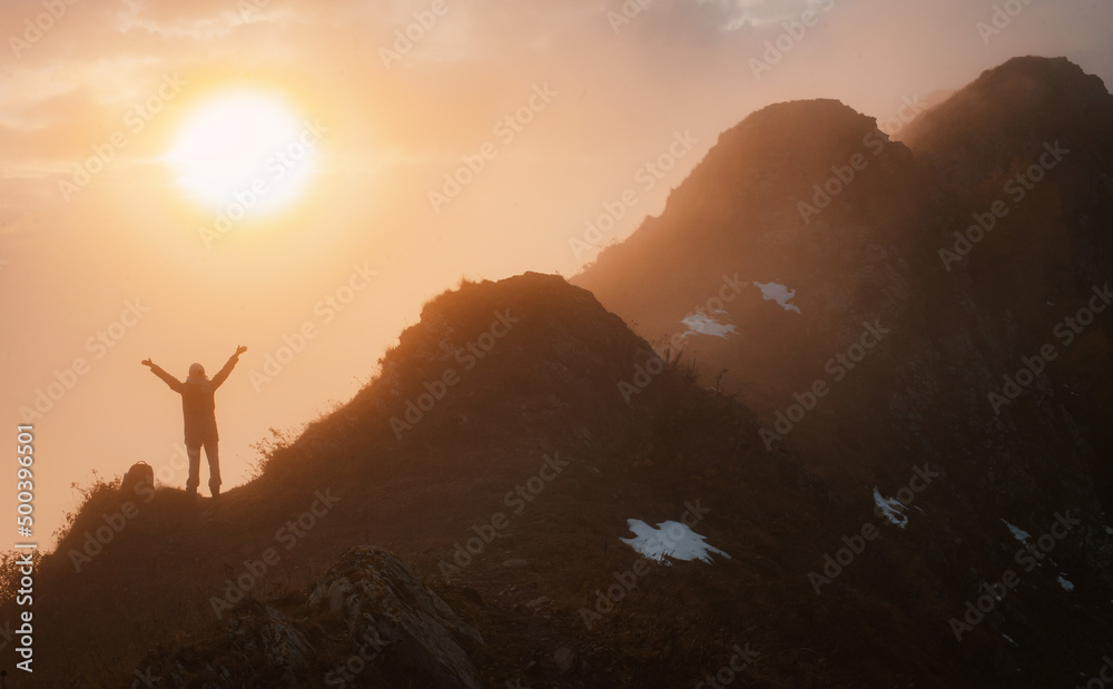 female tourist with a backpack in autumn on the mountain with outstretched arms welcomes admires the sunset