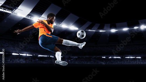 Young professional football or soccer player in motion on stadium with flashlights  kicking ball for winning goal. Concept of sport  competition  motion  overcoming.