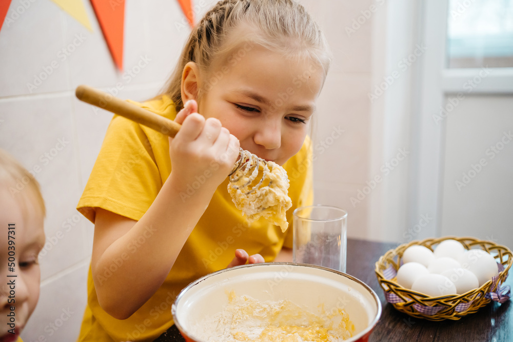 girl with her brother cooks and tastes dough, white eggs on the table, Easter holiday