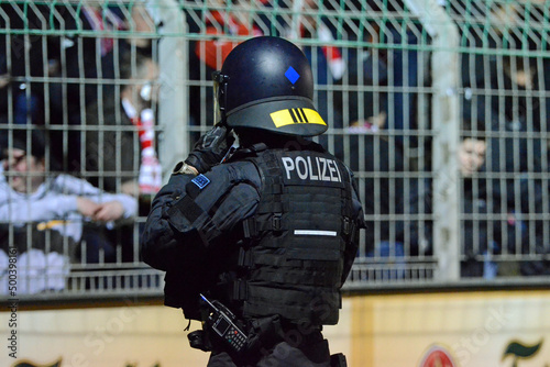 Symbolbild behelmter Bereitschaftspolizist zur Absicherung vor Fanblock im Fußballstadion