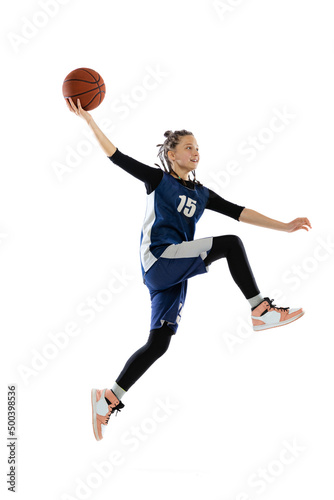 Portrait of teen girl in blue uniform training, playing basketball isolated over white background. Scoring winning goal © Lustre
