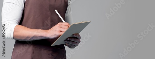 Fotografiet Handsome barista wearing apron writing order on clipboard