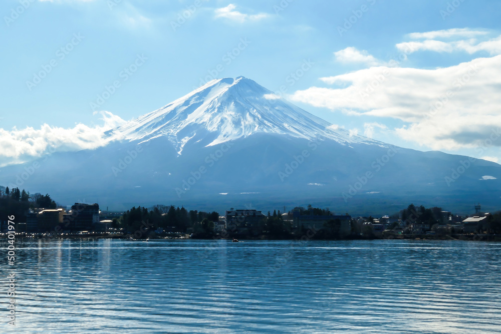 A close up view on Mt Fuji from the side of Kawaguchiko Lake, Japan. The mountain is hiding behind the clouds. Top of the volcano covered with a snow layer. Serenity and calmness. Calm lake's surface