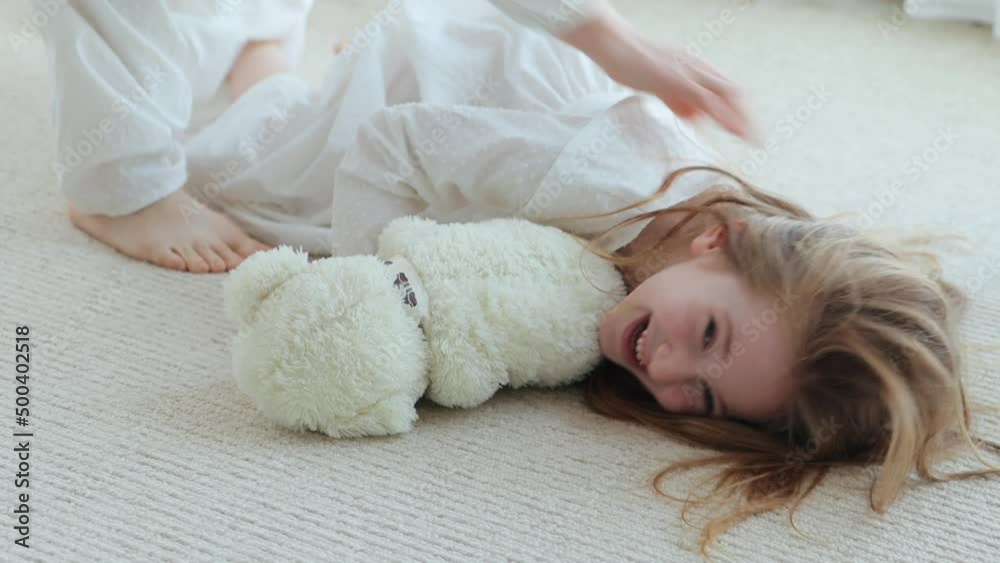 Young mother and little cute little girl dressed in white old fashioned pajamas having fun at home. Close-up of mother tickling daughter on the floor, 4k video Young mother and little cute little girl dressed in white old fashioned pajamas having fun at home. Close-up of mother tickling daughter on the floor, 4k video