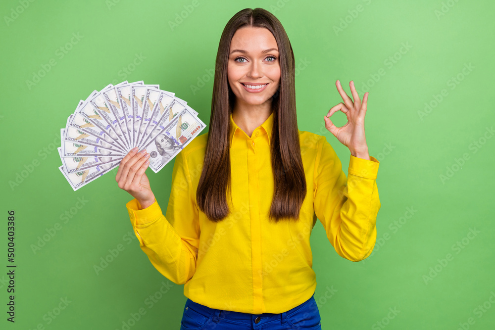 Photo of young cheerful girl show fingers okey symbol cash profit benefit recommend great isolated over green color background Photo of young cheerful girl show fingers okey symbol cash profit benefit recommend great isolated over green color background