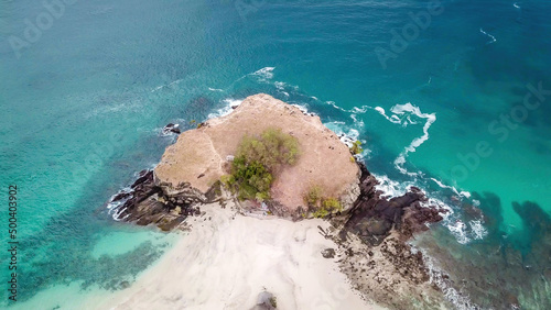 A top-down drone shot of an idyllic Koka Beach. Hidden gem of Flores, Indonesia. Headland going straight into the open sea. Beauty in the nature. Calm waves washing the cliff's slopes. Serenity.