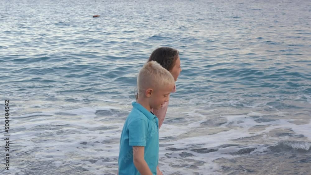 Brother and sister have fun and play on the beach, he walks along the shore and splashes water. Brother and sister have fun and play on the beach, he walks along the shore and splashes water.