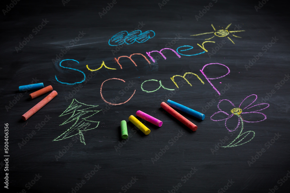 Text Summer camp written on black chalkboard, with chalk sticks of different colors Text Summer camp written on black chalkboard, with chalk sticks of different colors