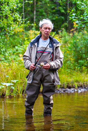 Portrait of fisherman in waders with spinning rod on the river. Spinning fishing