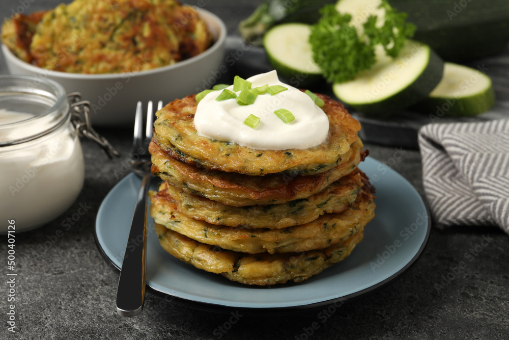 Delicious zucchini pancakes with sour cream and green onion served on grey table, closeup Delicious zucchini pancakes with sour cream and green onion served on grey table, closeup