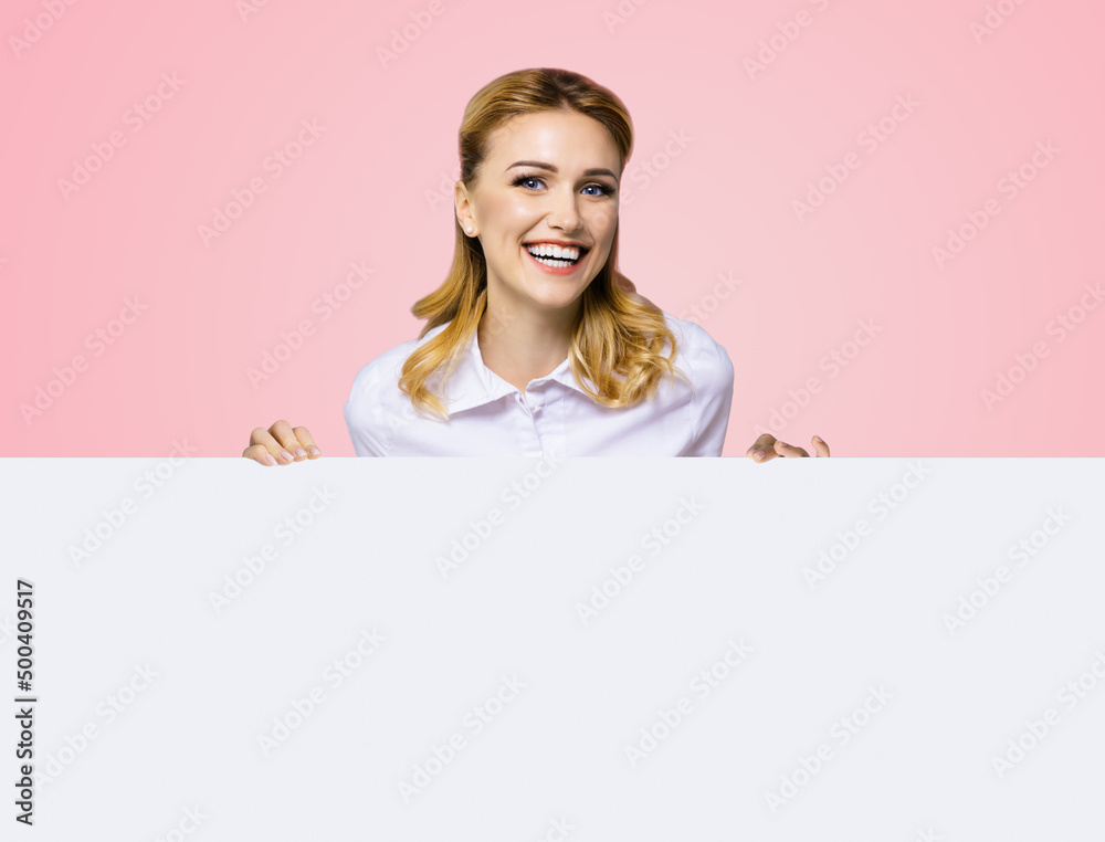 Very happy excited, laughing business woman in white confident clothing standing behind empty banner signboard with copy space text area. Rose pink color background. Advertising concept. Very happy excited, laughing business woman in white confident clothing standing behind empty banner signboard with copy space text area. Rose pink color background. Advertising concept.