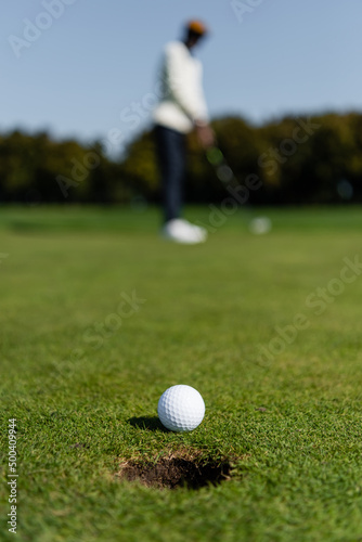 golf ball on grass of green field near blurred golfer.