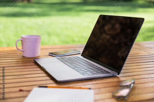 Computer, tazza, quaderno e occhiali su tavolo di legno in un giardino d'estate  photo