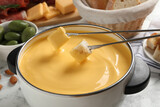 Pot of tasty cheese fondue and forks with bread pieces on white table, closeup