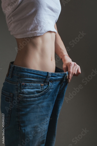 young woman dressed in wide jeans and a white shirt, demonstrates successful weight loss. concept of diet and weight loss